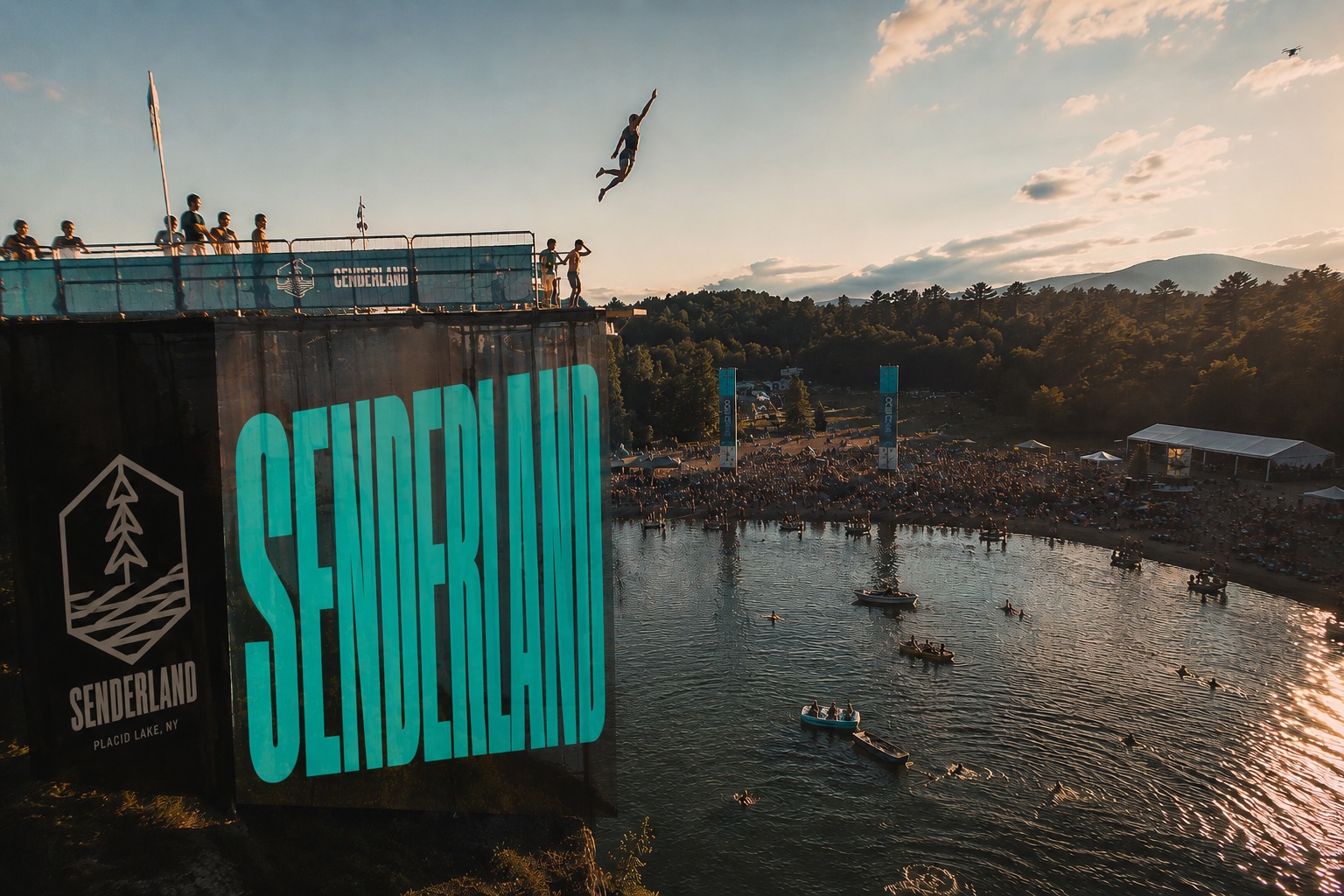A diver leaps from the SenderLand tower above the festival crowd at golden hour