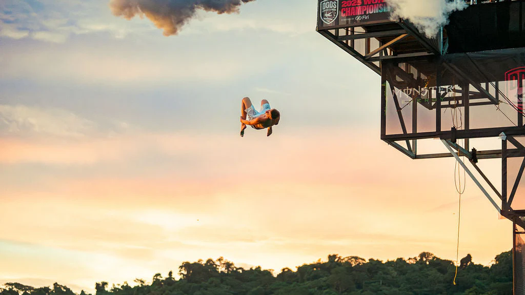 Cliff diver mid-flip at dusk above the Senderland skyline